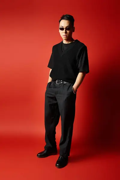 Stock image A stylish and handsome Asian man in black attire striking a pose in front of a vivid red background in a studio setting.