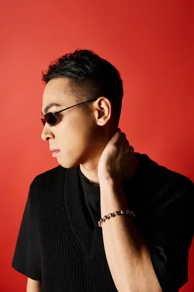 stock image A handsome Asian man exudes style in a black shirt and sunglasses against a vibrant red background in a studio setting.