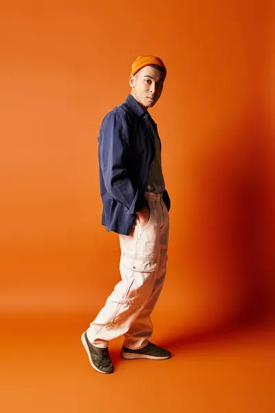 ハンサムなアジア人男性はスタジオの設定で活気に満ちたオレンジ色の背景に対してスタイリッシュな服装で自信を持って立っています — ストック写真