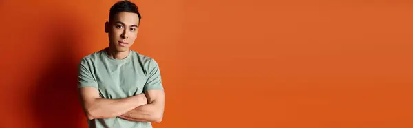 Stock image A handsome Asian man wearing stylish attire confidently stands in front of a vibrant orange wall in a studio setting.