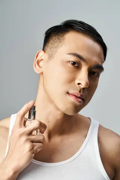 Handsome Asian Man White Tank Top Spraying Perfume Grey Studio Stockfoto