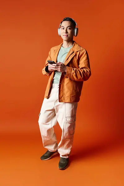 Stylish Asian Man Stands Front Bold Orange Background Wearing Headphones — Stock Photo, Image