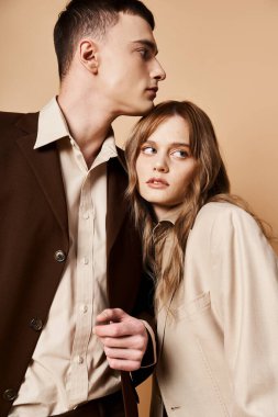 Zarif takım elbiseli çekici çift sevgiyle poz veriyor ve pastel arka planda kameraya bakıyor.