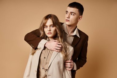 Sofistike, güler yüzlü bir adam kameraya bakan güzel kız arkadaşının yanında poz veriyor.