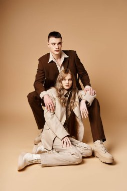 Pastel takım elbiseli çekici bir kadın kameraya bakıyor ve yakışıklı erkek arkadaşının yanında oturuyor.