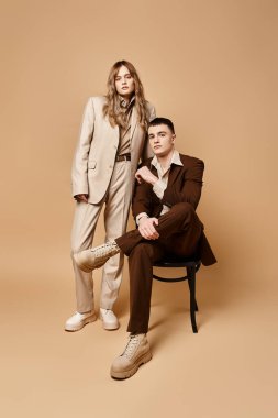 Sofistike takım elbiseli çekici bir çift birlikte poz veriyor ve pastel arka planda kameraya bakıyor.