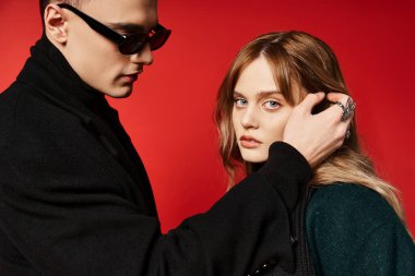 Uzun saçlı, zarif bir kadın. Erkek arkadaşının yanında güneş gözlüklü kameraya bakıyor.