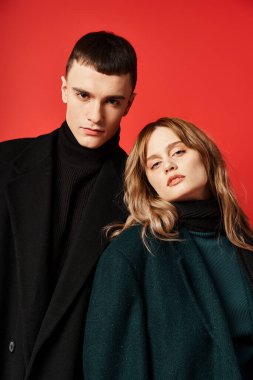 Entellektüel ceketli, kırmızı renkli arka planda kameraya bakan sevgi dolu bir çift.