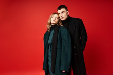 Zarif ceketli, şık bir çift birlikte poz veriyor ve canlı arkaplana bakıyor.