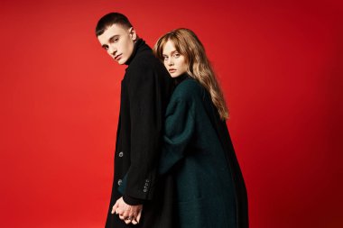 Cazibeli kadın kameraya bakıyor ve sevgilisiyle kırmızı arka planda poz veriyor.