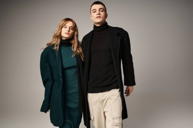 Gri arka planda poz verip kameraya bakan moda erkek ve kız arkadaş.