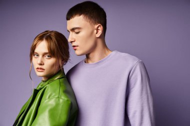 Yeşil elbiseli güzel kız arkadaşı mor kazaklı erkek arkadaşının yanında kameraya bakıyor.