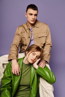 İyi giyimli, yeşil canlı giyinmiş bir kadın çekici erkek arkadaşının yanındaki kameraya bakıyor.