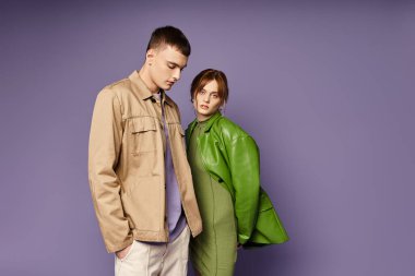 Yeşil ceketli çekici kadın mor arka planda sevgili erkek arkadaşının yanında kameraya bakıyor.