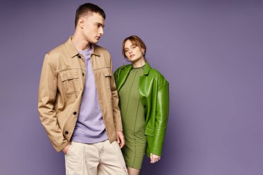 alluring woman in green jacket looking at camera near her loving boyfriend on purple backdrop clipart