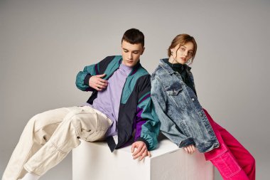 beautiful woman in fashionable bomber looking at camera next to her handsome boyfriend on white cube clipart