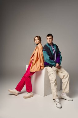 Canlı, şık bombardıman uçaklarıyla beyaz kübün üzerindeki gri arkaplanda kameraya bakan ilgili ve modaya uygun bir çift.