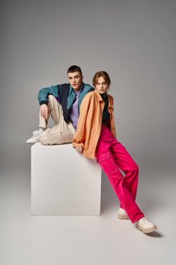 loving appealing couple in vivid stylish bombers looking at camera on gray backdrop on white cube clipart