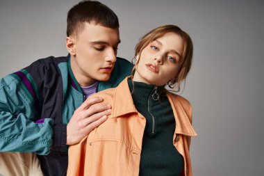 Gri arka planda yakışıklı erkek arkadaşının yanındaki kameraya bakan şık bombardıman uçağı içindeki çekici kadın.