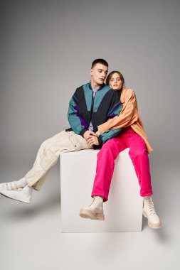 appealing woman in fashionable bomber looking at camera next to her handsome boyfriend on white cube clipart