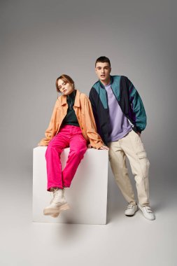 loving appealing couple in vivid stylish bombers looking at camera on gray backdrop on white cube clipart