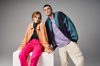 Canlı stil bombardıman uçaklarıyla beyaz kübün üzerindeki gri arkaplanda kameraya bakan çekici bir çift.