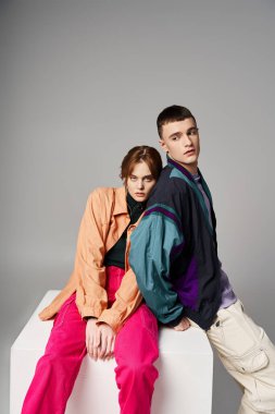 appealing woman in fashionable bomber looking at camera next to her handsome boyfriend on white cube clipart