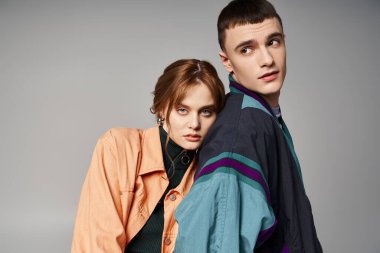 Gri arka planda yakışıklı erkek arkadaşının yanındaki kameraya bakan şık bombardıman uçağı içindeki çekici kadın.