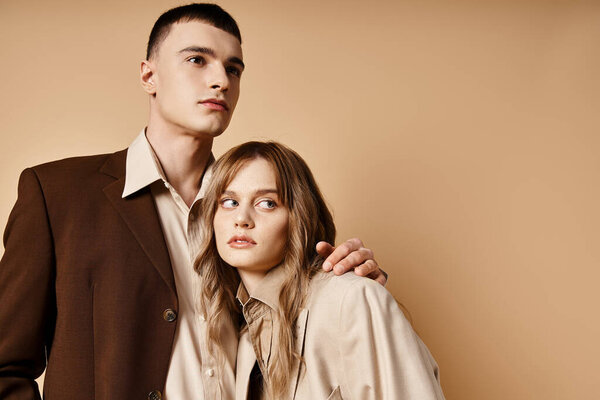 appealing debonair couple in elegant suits posing lovingly and looking at camera on pastel backdrop