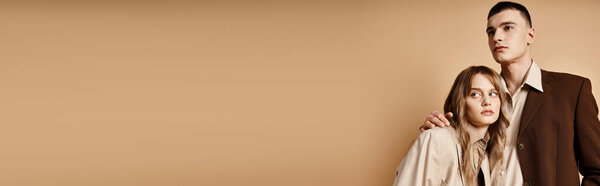 passionate debonair couple in elegant suits posing and looking at camera on pastel backdrop, banner