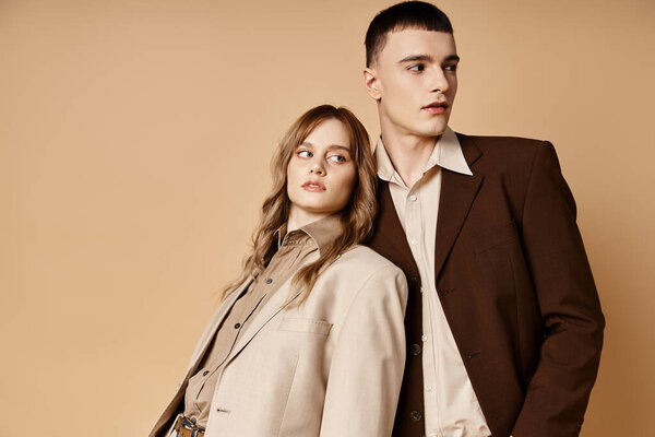 appealing debonair couple in elegant suits posing lovingly and looking at camera on pastel backdrop