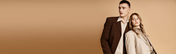 passionate debonair couple in elegant suits posing and looking at camera on pastel backdrop, banner