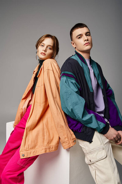 caring appealing couple in vivid stylish bombers looking at camera on gray backdrop on white cube