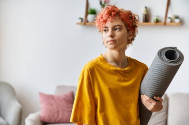 Kızıl saçlı, canlı giyinmiş, yoga minderini tutan ve başını çeviren güzel, güzel, tuhaf bir kız.