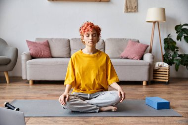 Ateşli sarı tişörtlü, kızıl saçlı, evde meditasyon yapan, abartılı, tuhaf, çekici bir adam.