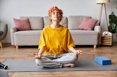 Güzel, savurgan, tuhaf, kızıl saçlı, parlak sarı tişörtlü, evde meditasyon yapan biri.