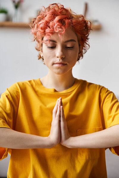 appealing young queer person in vivid yellow t shirt sitting on mat and doing some yoga at home