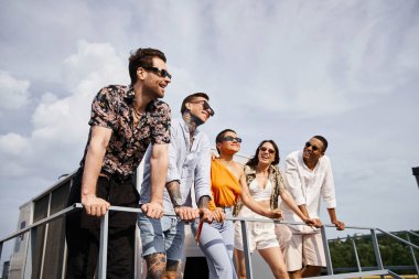 Neşeli, çekici, ırklar arası, canlı giysiler içinde çatıda poz veren ve başka tarafa bakan arkadaşlar.