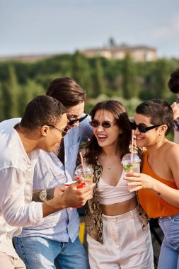 cheerful multiracial friends with trendy sunglasses drinking cocktails next to DJ at rooftop party clipart