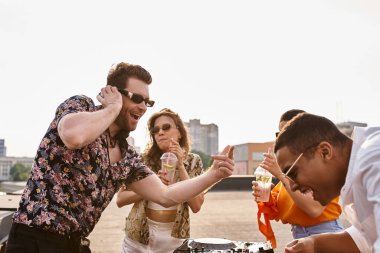 Neşeli ırklar arası güzel arkadaşlar çatıdaki partide kokteyl içip DJ 'lik yaparak dans ediyorlar.