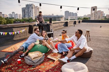 Şık şehir kıyafetleri içinde çok kültürlü genç arkadaşlar çatıda kokteyllerle bardaklarını tokuşturuyorlar.