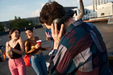 Kulaklıklı DJ 'e odaklan. Arka planda bulanık arkadaşlarıyla çatıdaki partide eğleniyor.
