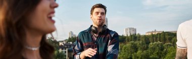 focus on handsome cheerful DJ playing music for his blurred jolly friends at rooftop party, banner clipart