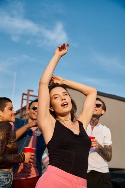 Çatıdaki partide bulanık arkadaşlarının yakınındaki kameraya bakan neşeli güzel kadına odaklan.