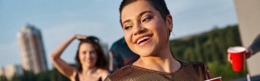 cheerful shorthaired woman with braces looking away with her blurred friend on backdrop, banner clipart