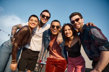 Çatı katındaki partide kameraya gülümseyen şık elbiseli, güzel ırklar arası arkadaşlar.