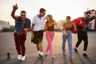 Neşe dolu ırklar arası, güneş gözlüklü, alkollü ve çatı katındaki partide koltuk koltuğu olan arkadaşlar.