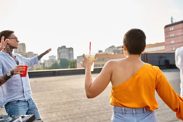 short haired young woman with cocktail in hand partying on rooftop with her tattooed friend