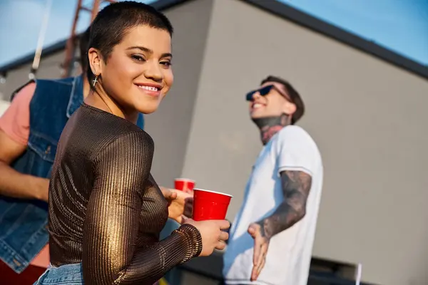 stock image merry short haired woman in vivid outfit holding cocktail and having fun next to her diverse friends