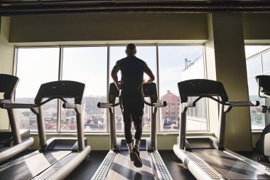 Formda bir adam spor salonundaki koşu bandında koşar. Egzersiz rutinine enerji ve efor harcar..